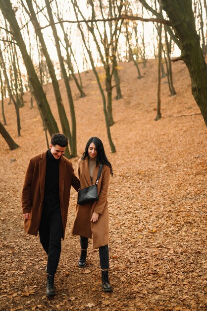 Two people walking through a park in the fall, wearing outfits featuring earthy tones like brown, green, and orange.