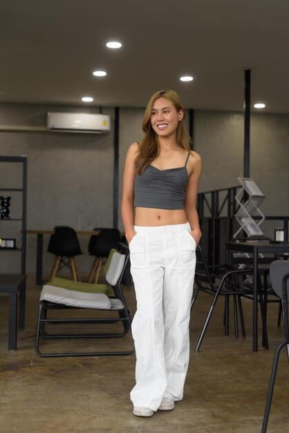 A woman with an inverted triangle body shape wearing a dark-colored top with a V-neck, paired with wide-leg pants and pointy-toe heels. The setting is a modern office space.