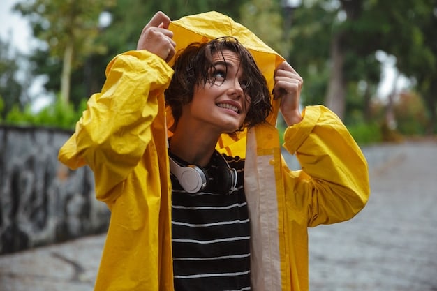 A person wearing a waterproof jacket standing in the rain. The jacket is brightly colored and the rain is visible as droplets on the fabric. The background is blurred to focus on the jacket and the rain.