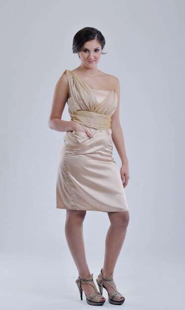 A woman wearing a little black dress with a neutral-colored scarf draped asymmetrically over one shoulder. She's wearing strappy heels and delicate jewelry.