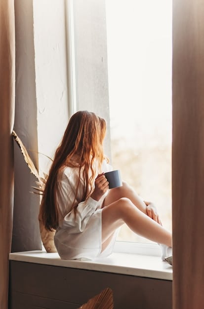 A person sitting by a window in the morning, bathed in natural sunlight, enjoying a cup of tea. The room is bright and airy.