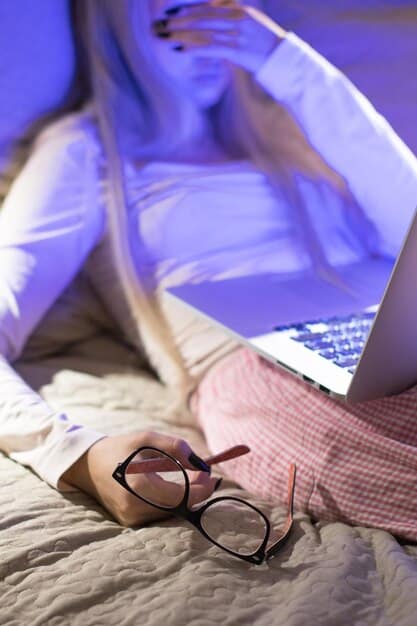A person wearing blue light-blocking glasses while using a laptop in a dimly lit room, with a soft, warm light emanating from the screen.