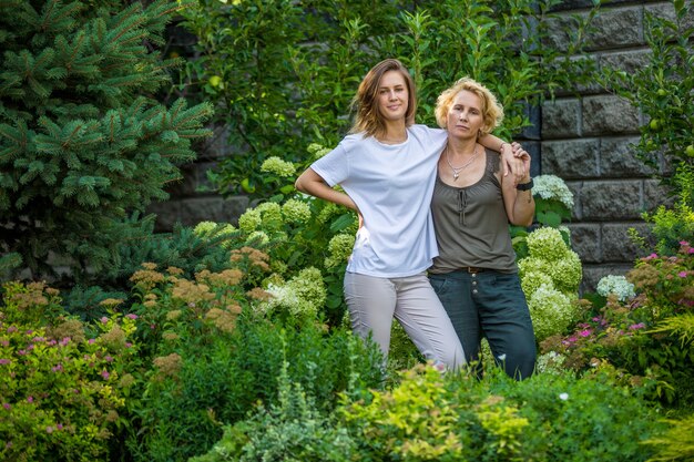 Two senior women laughing and talking while walking together in a park, with trees and greenery in the background. They appear to be close friends enjoying each other's company.