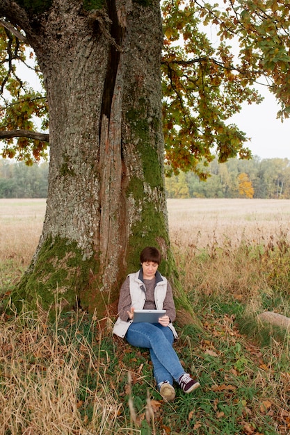 A person sitting quietly under a tree in a forest, with a notebook and pen in hand, appearing to be deep in thought. The scene should convey a sense of calm reflection and creativity, highlighting the link between nature and mental clarity. Focus on the individual's relaxed posture and the surrounding natural elements.