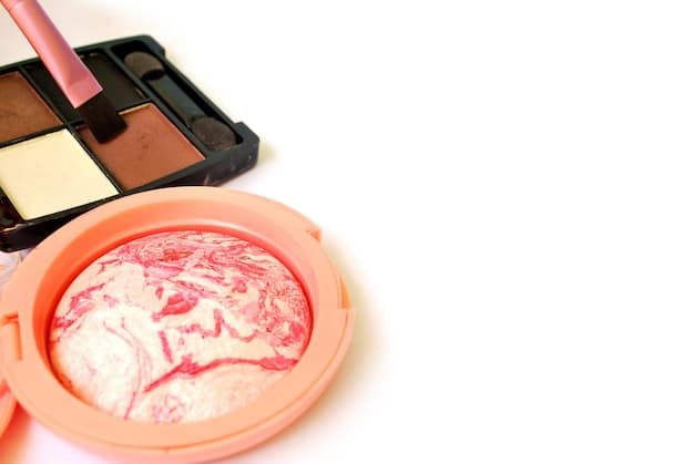 A close-up of various makeup products in shades of peach, including eyeshadows, a blush compact, and lipstick tubes displayed in an organized manner.
