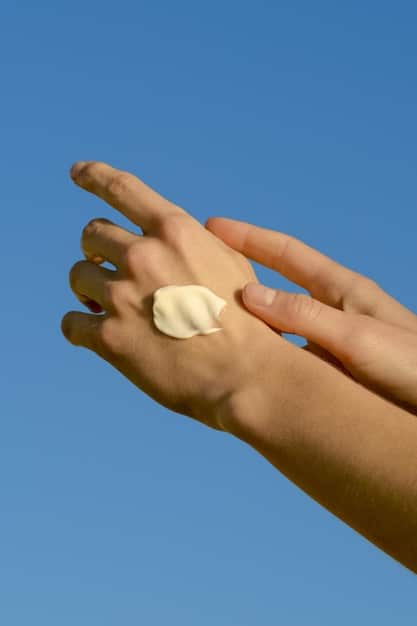 A close-up shot of sunscreen being applied to a hand, with a focus on the texture and coverage of the product. The background is a blurred image of a sunny outdoor scene.